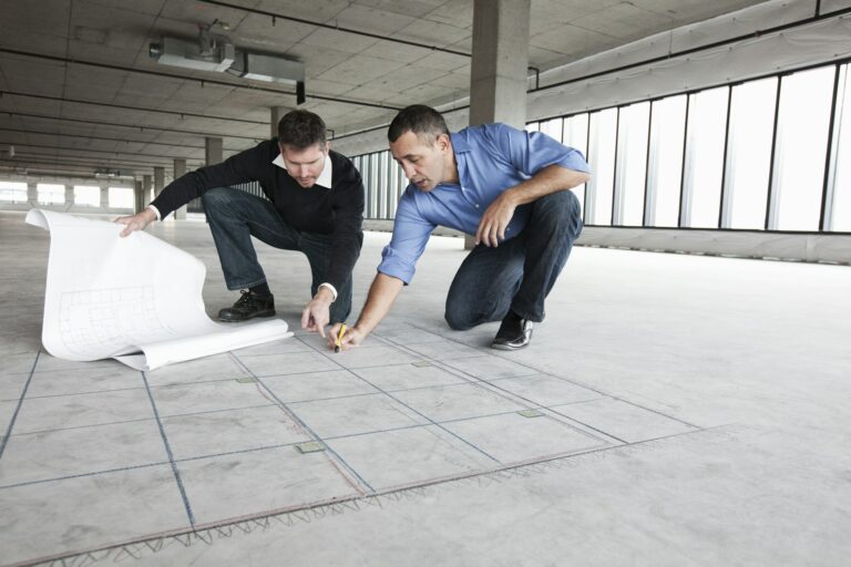 An architect and a business owner crouching over architectural plans planning new offices